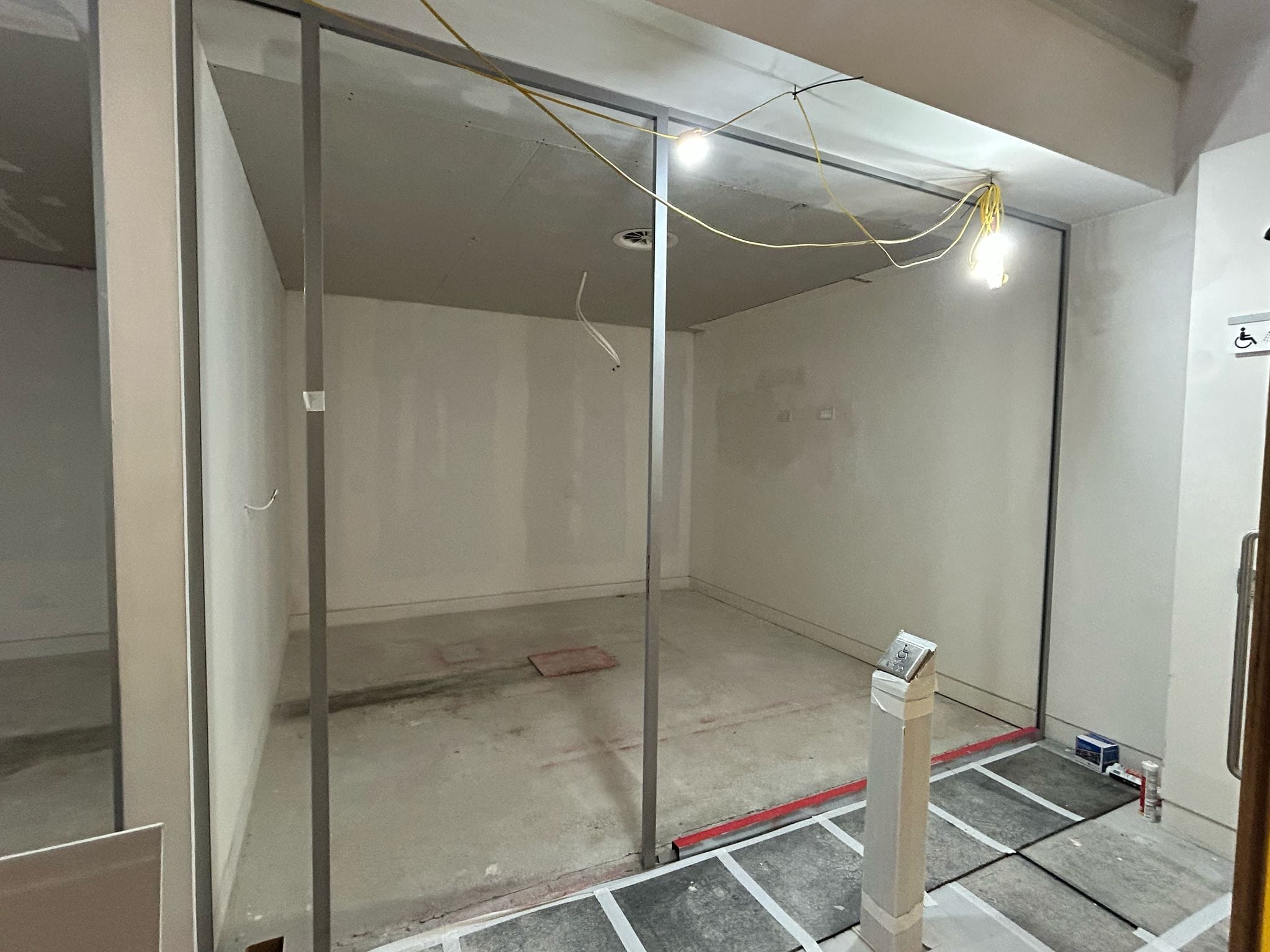 A new meeting room has been built. The front of the room has sliding glass doors, the walls and flooring is unfinished, wires hang down from the ceiling.